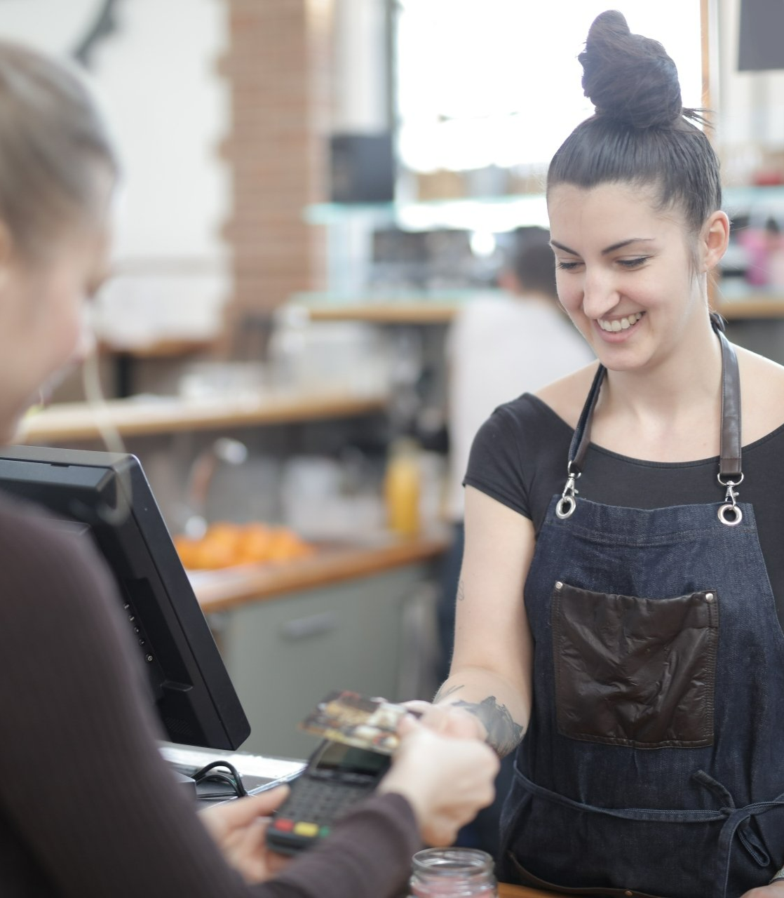 A woman in a denim apron is smiling at a customer