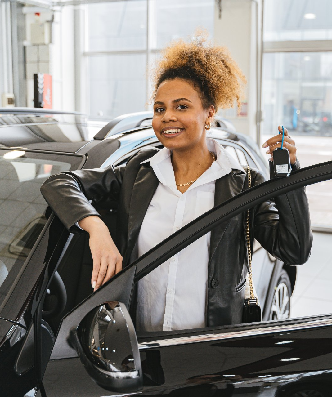 A woman is standing next to a car in a showroom holding a car key.