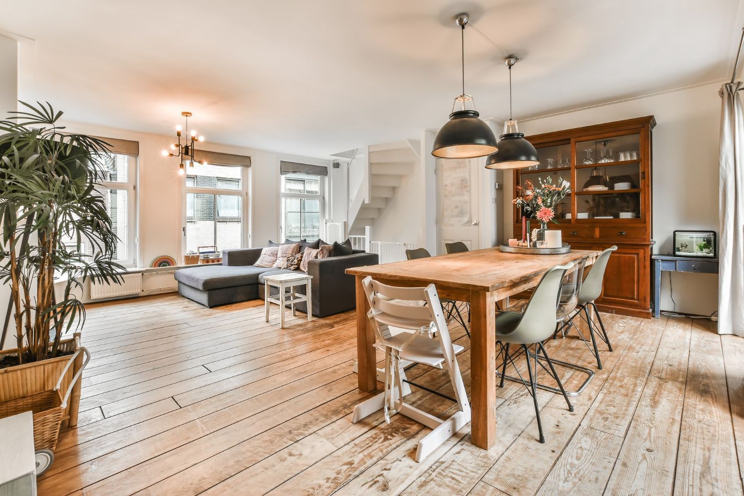 A bright, open-plan living and dining room with wooden floors, a large dining table, and a sofa in the background.