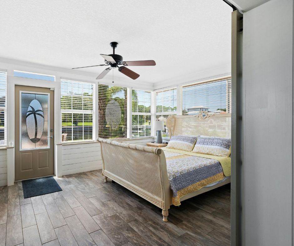 A sunroom bedroom with wooden flooring, a bed with blue and yellow bedding, and a door featuring a palm tree design.