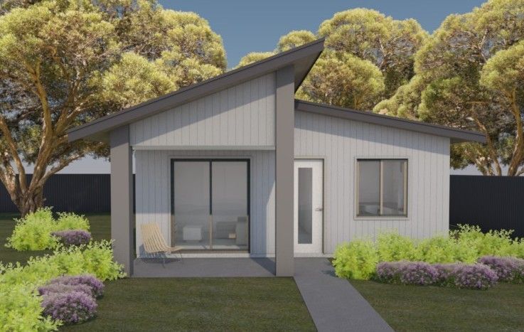 A light-gray single-story house with a sloped roof, a sliding glass door, and a grassy yard with small bushes.
