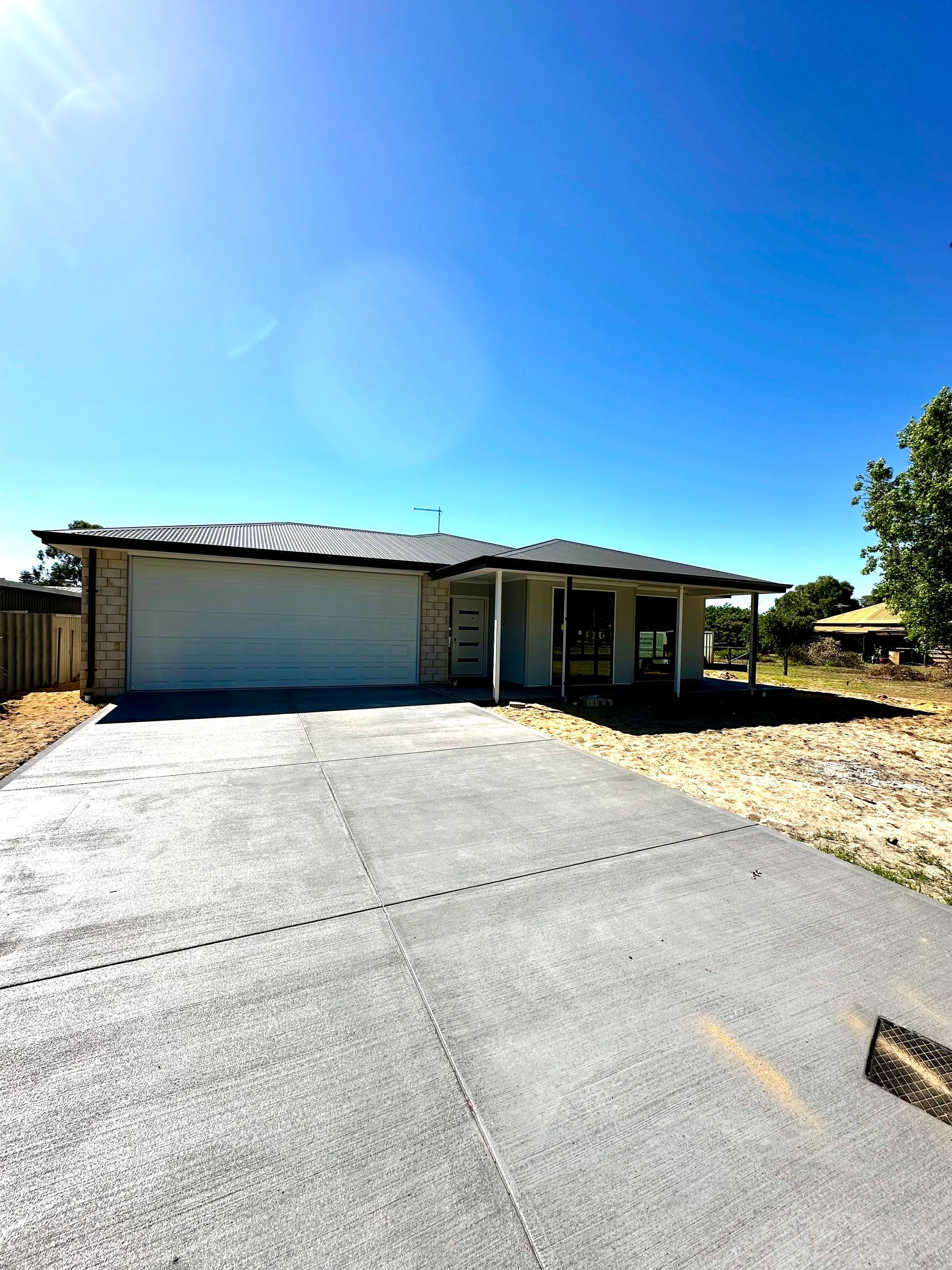 Single-story residential house with a large concrete driveway and garage, under a bright blue sky.