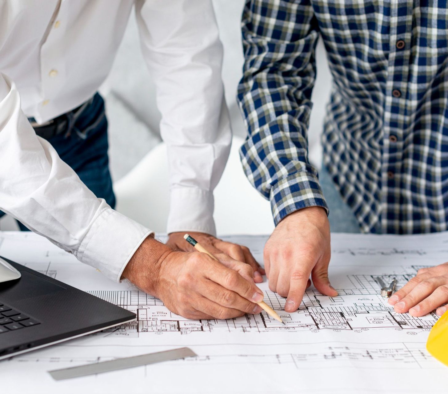 Two people in professional attire review architectural blueprints on a desk, one pointing while the other uses a pencil.