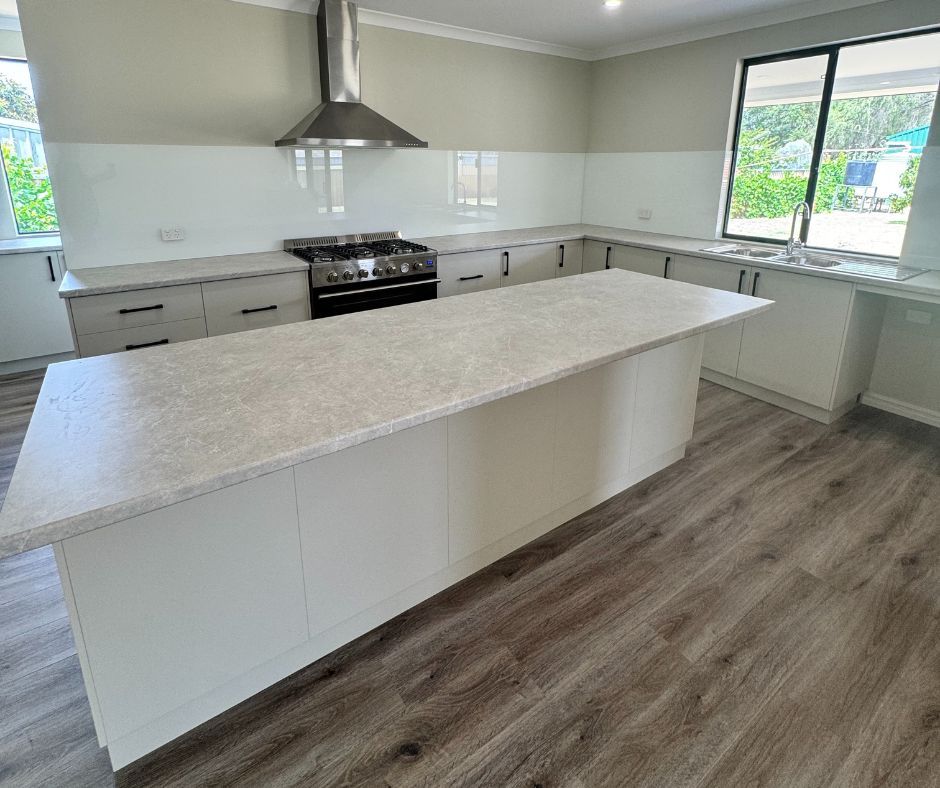 A modern, spacious kitchen featuring a large white island, light-colored countertops, white cabinetry, and wood floors.