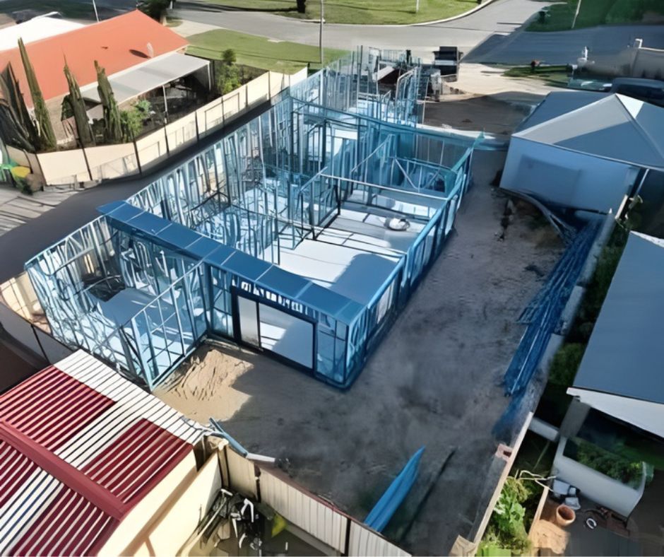 An aerial view of a residential construction site featuring a newly erected blue light-gauge steel frame for a house.