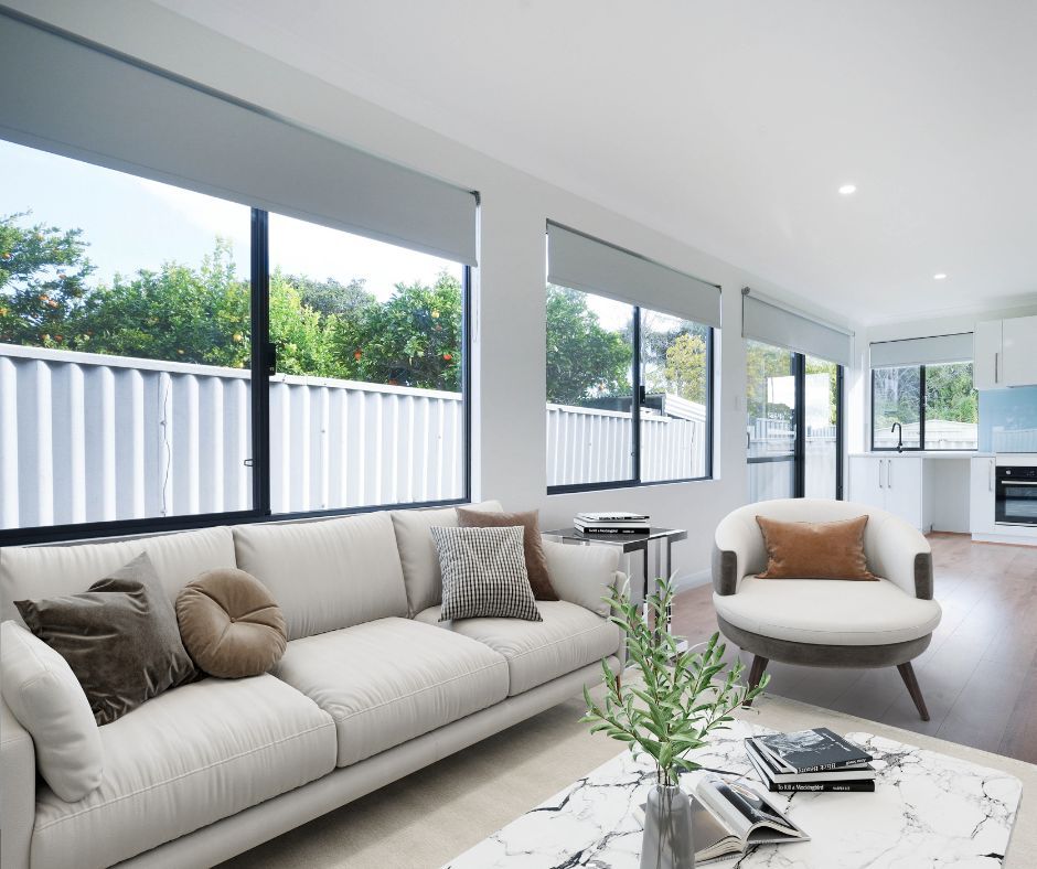 A bright living room with a light sofa, a circular armchair, a marble coffee table, and large windows with gray blinds.