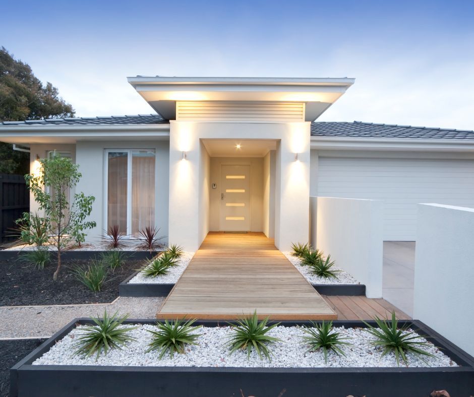 A modern, light-colored home featuring a wooden walkway leading to a front door with horizontal glass panels.