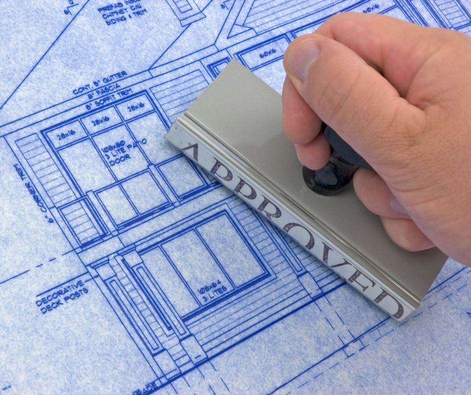 Hand stamping “APPROVED” on a blue architectural blueprint drawing