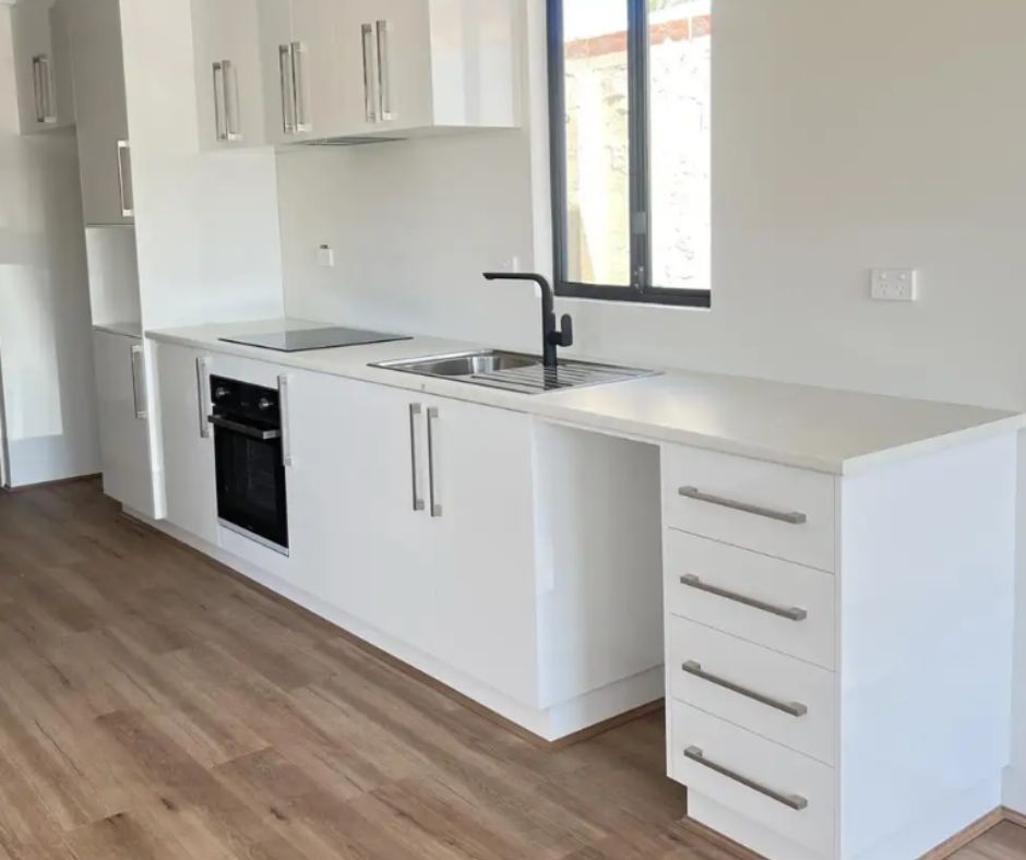 A modern kitchen with white glossy cabinets, light countertops, black fixtures, a built-in oven, and wood-look flooring.