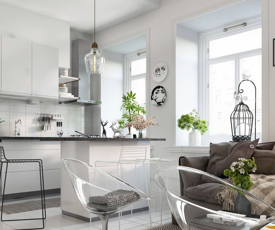 A modern, open-concept kitchen with white cabinetry, a glass pendant light, transparent chairs, and a cozy sofa area.