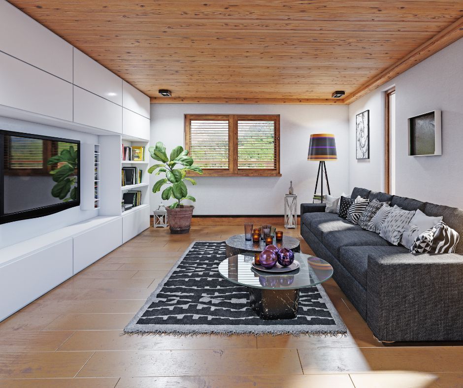 Modern living room with a large gray sofa, glass coffee tables, a patterned rug, and white built-in shelving with a TV.