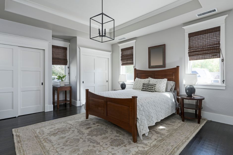 A neutrally decorated bedroom featuring a dark wood bed frame, white bedding, gray walls, two side tables, and a rug.