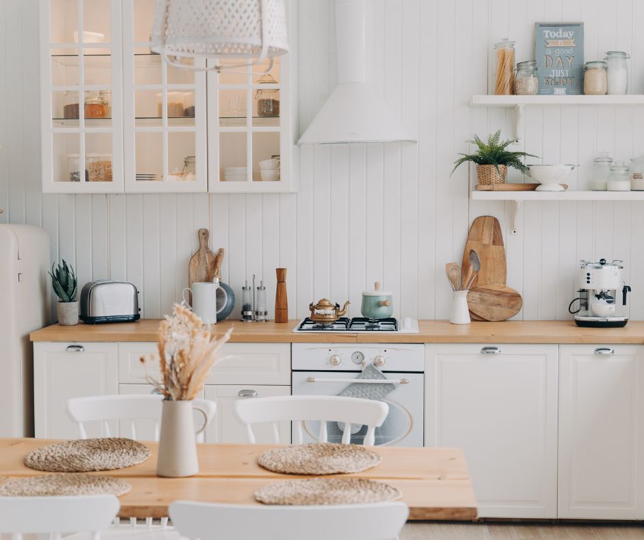 A brightly lit kitchen with white cabinetry, a wood countertop, and a wooden dining table with place settings.