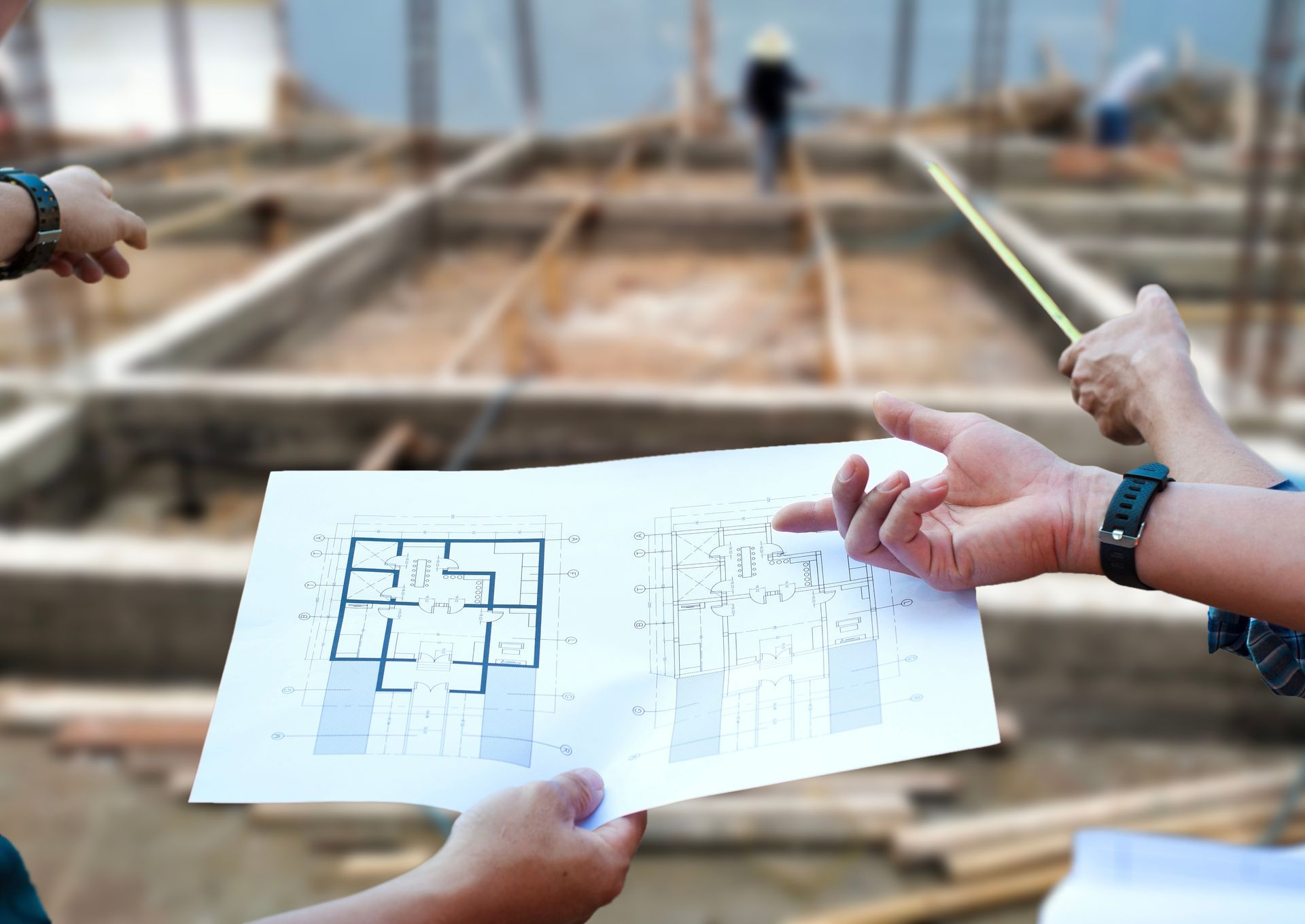 Hands holding a blueprint at a construction site with wooden framing in the background