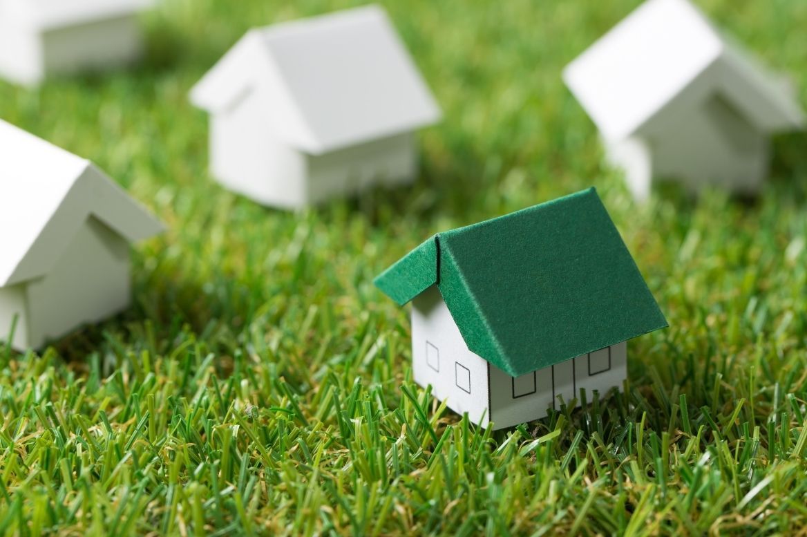 A small model house with a green roof sits in a patch of grass surrounded by white model houses.