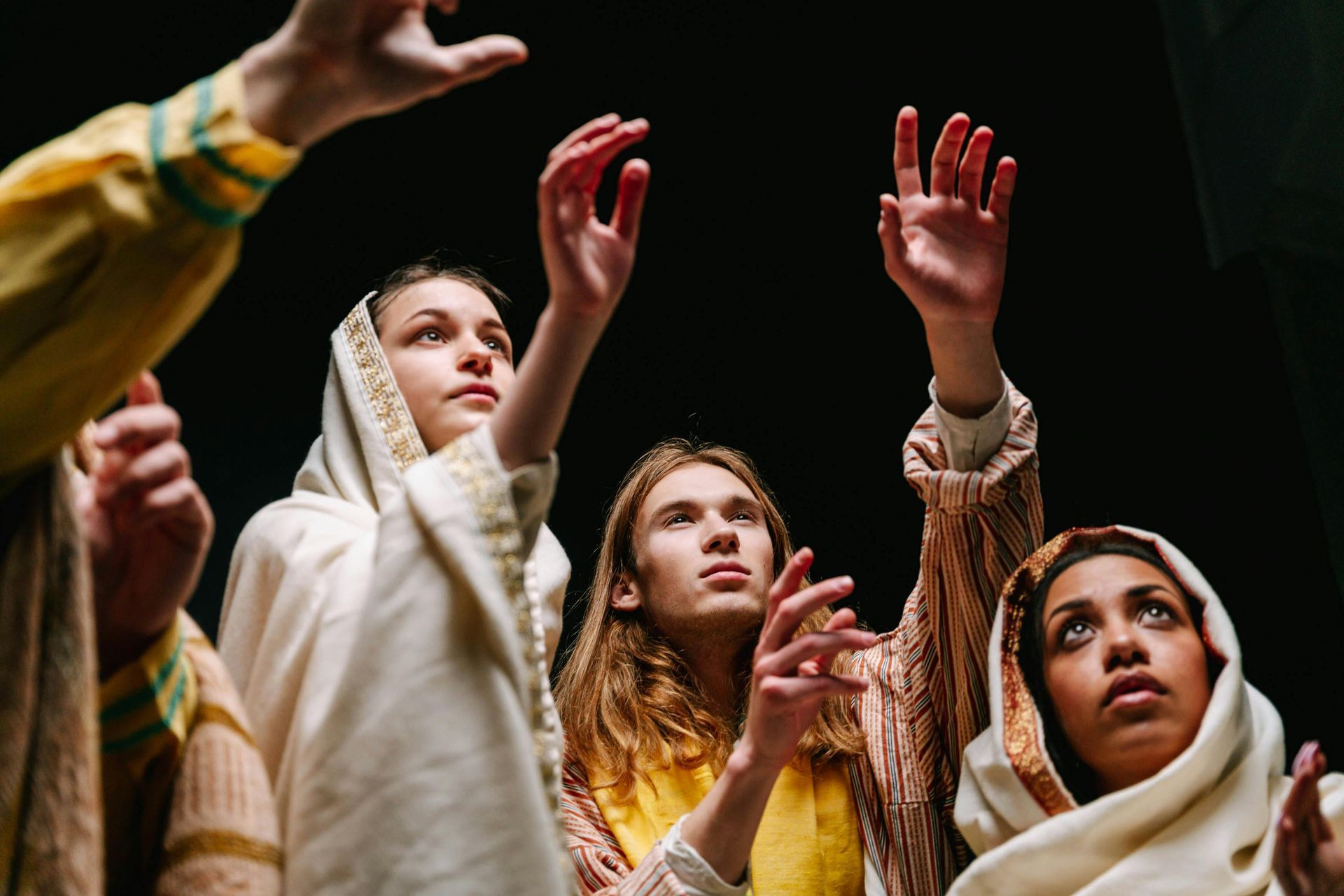 People with hands raised, wearing robes, looking upwards.