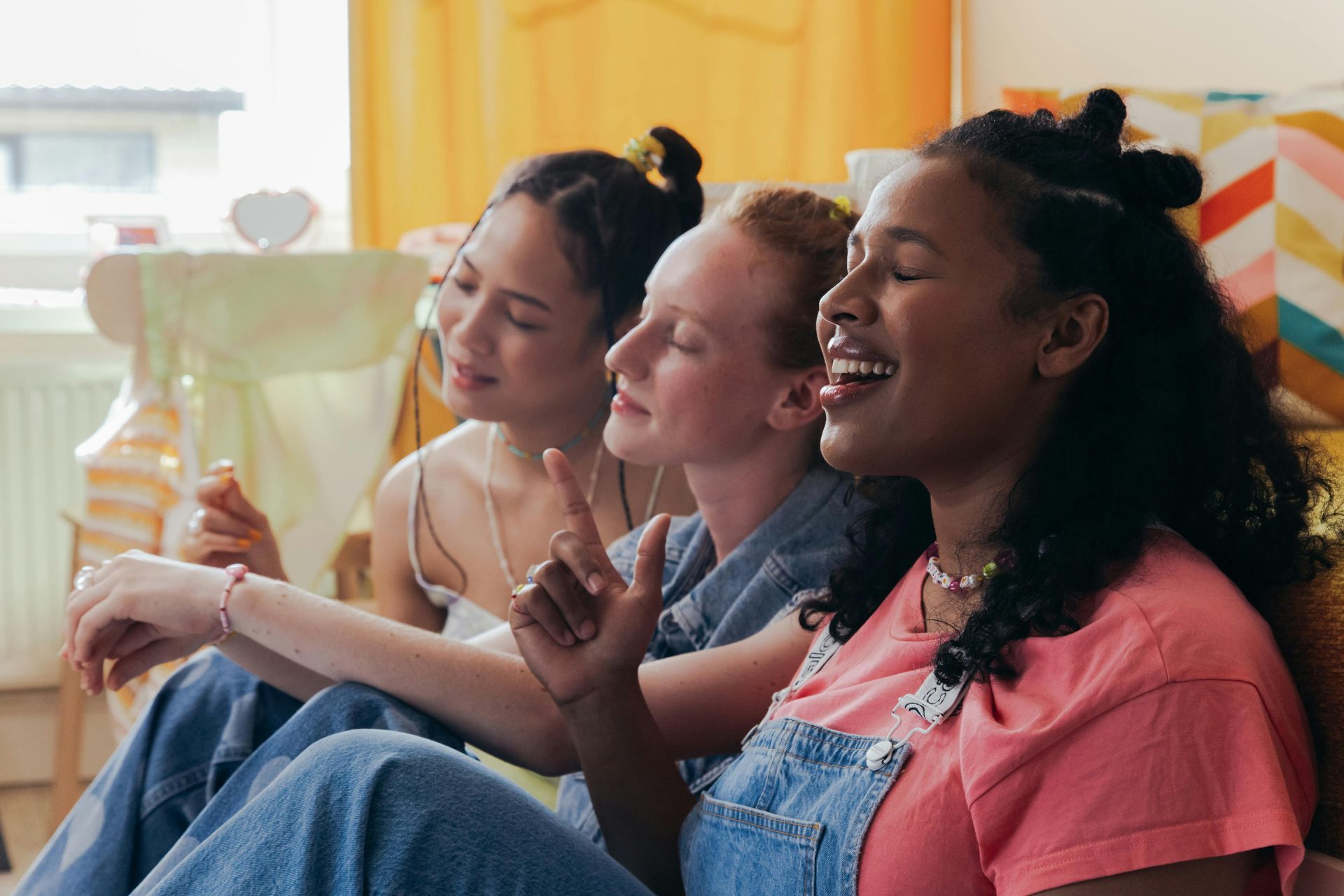 Three young women singing together, close-up, laughing with eyes closed; indoors.