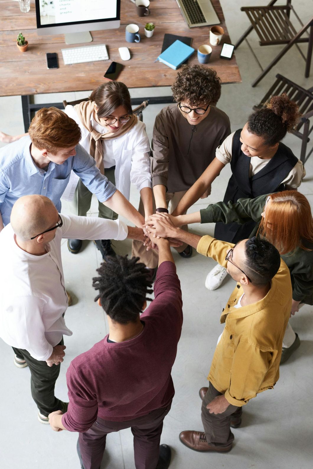 Group of diverse people in a circle with hands stacked, symbolizing teamwork and unity in an office setting.
