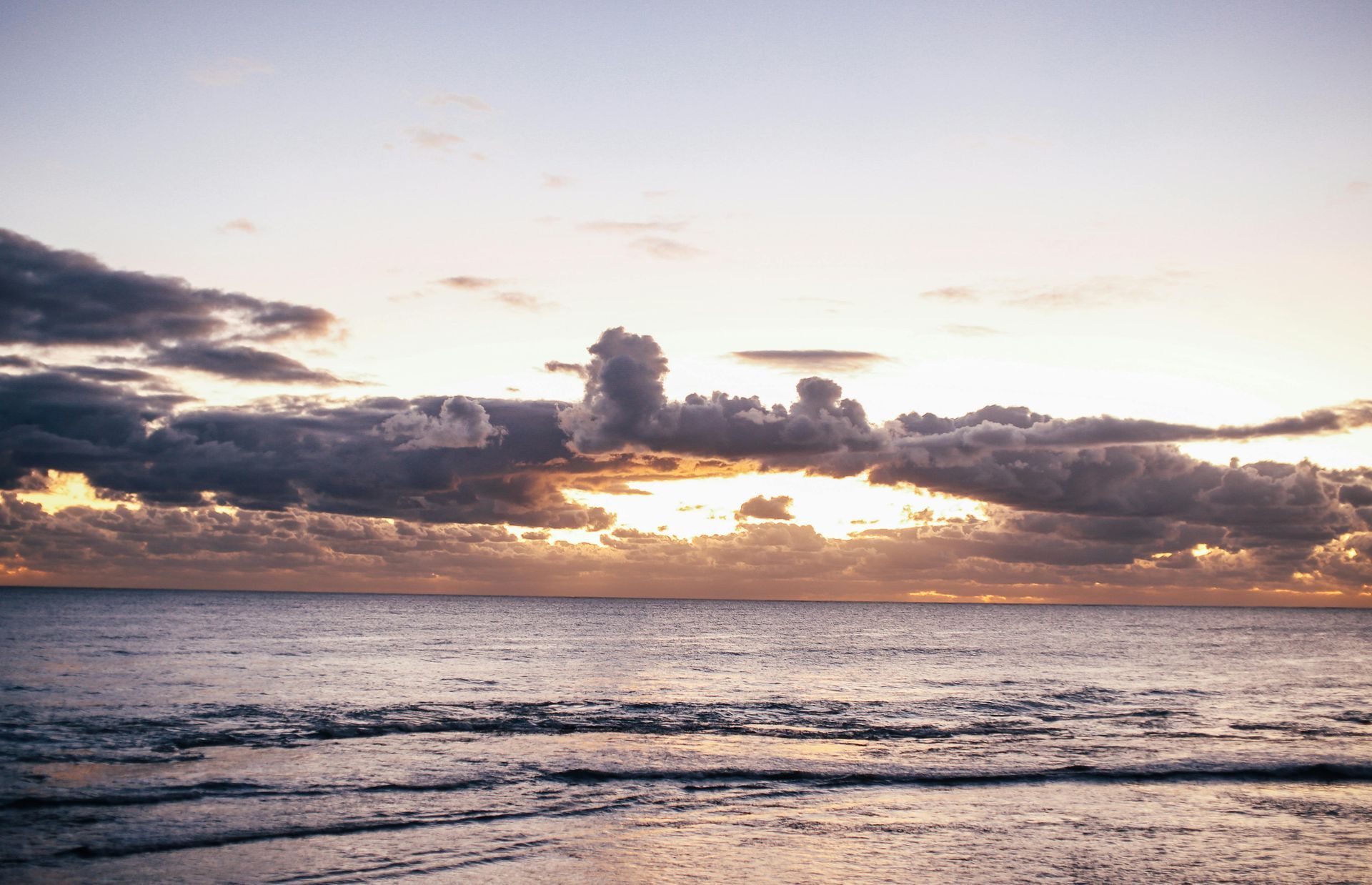 Ocean sunset with cloudy sky. Warm light breaks through clouds, reflecting on water.