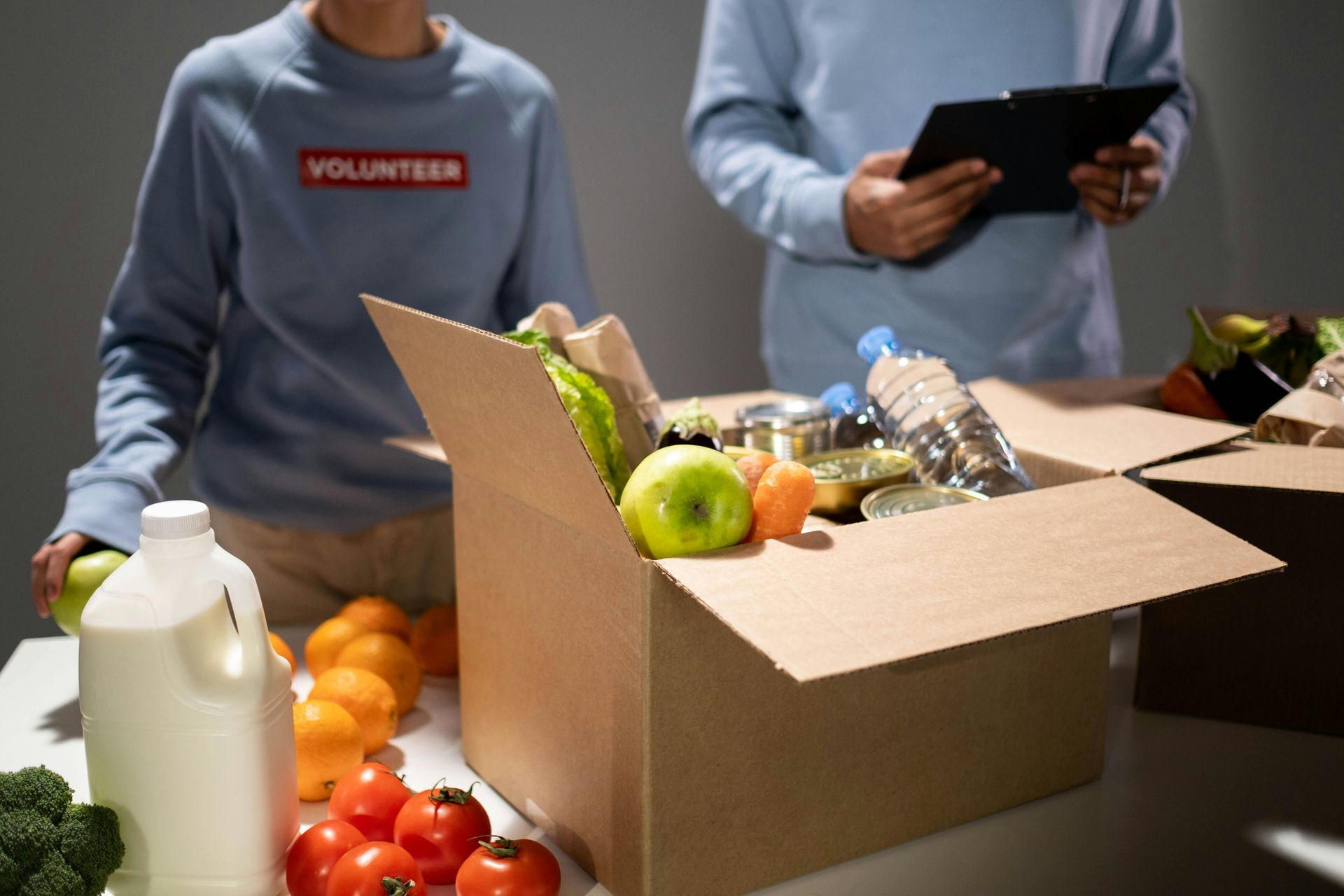 Volunteers packing a box of groceries, including fruits, vegetables, and canned goods.