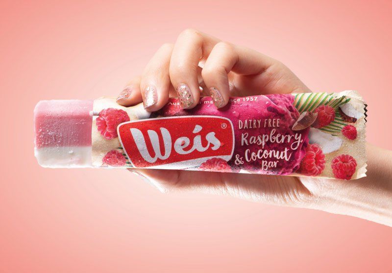 A person is holding a raspberry and coconut weis bar in their hand.