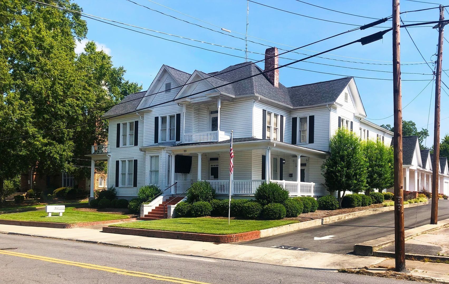 White Victorian house with black shutters, trees, and power lines.