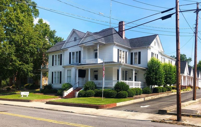 White Victorian house with black shutters, trees, and power lines.