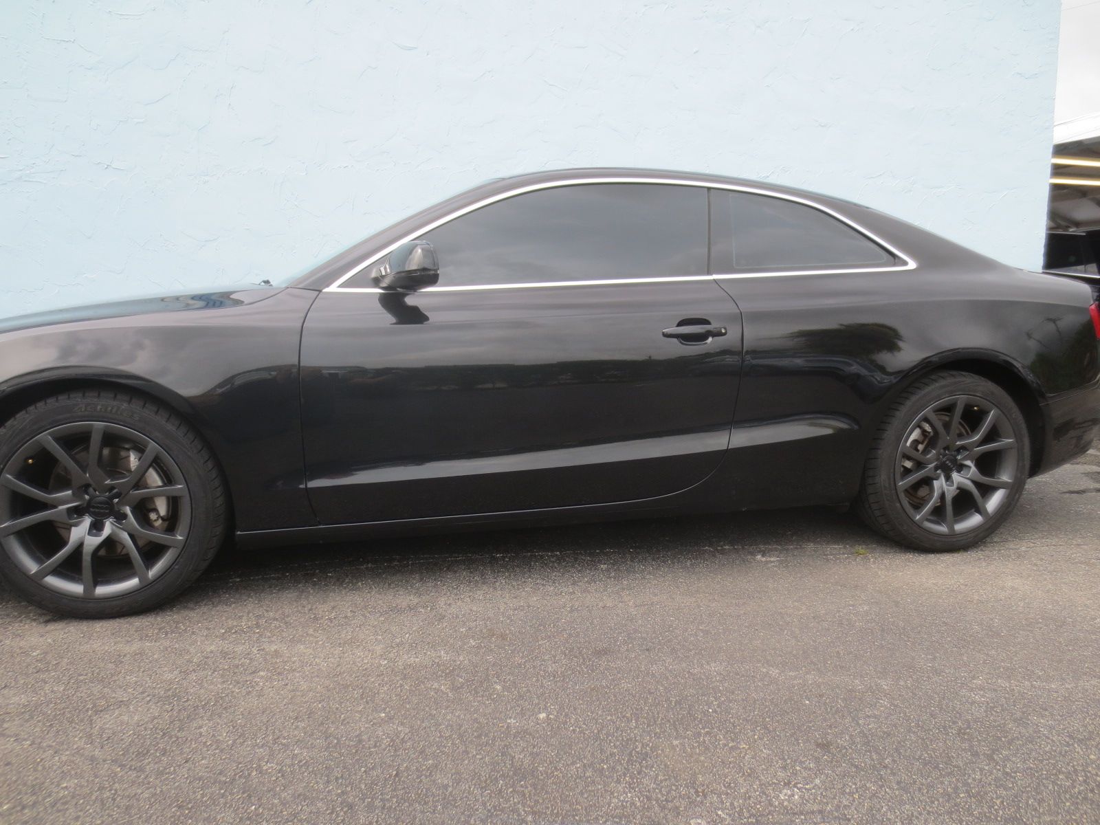 A black car is parked in front of a blue wall | B & R Auto Body Works