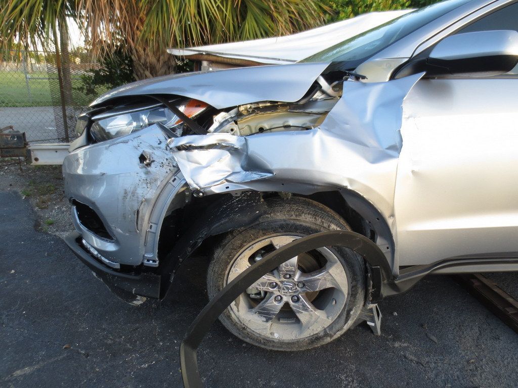 A silver car with a damaged front end is parked on the side of the road | B & R Auto Body Works