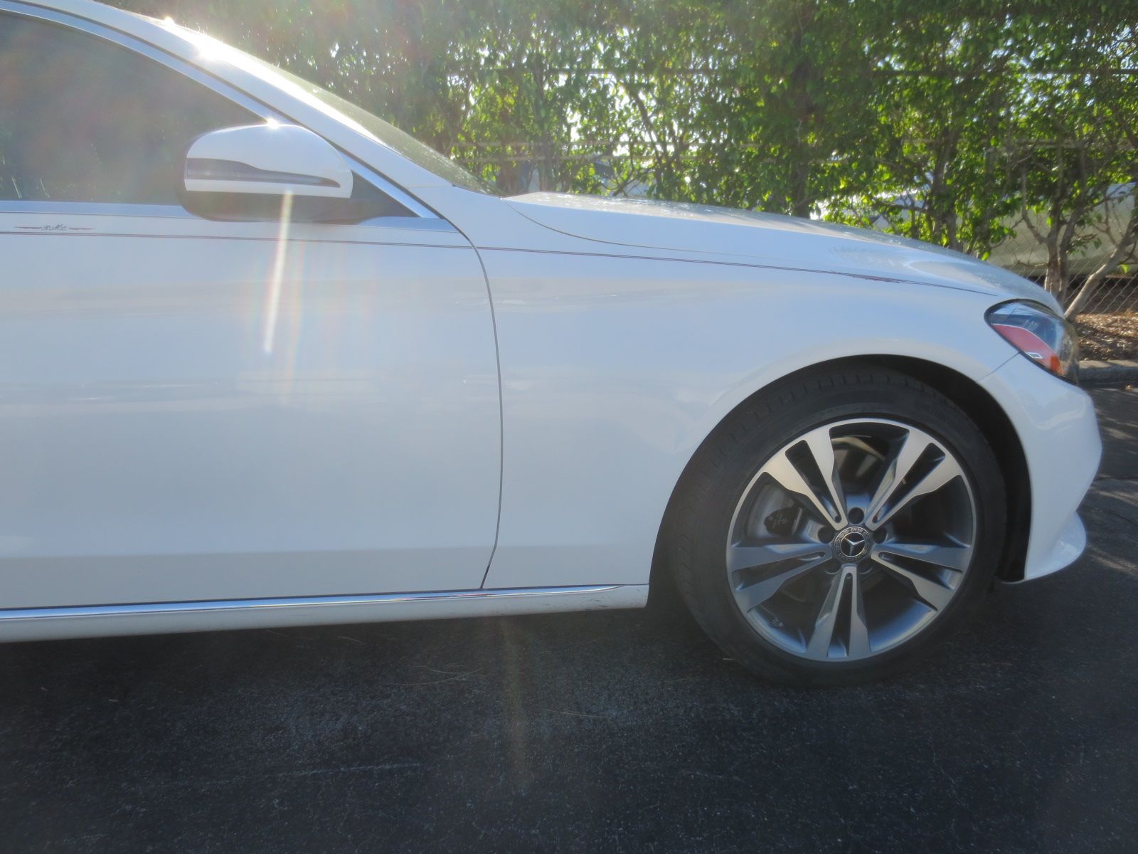 A white car is parked in a parking lot with trees in the background | B & R Auto Body Works