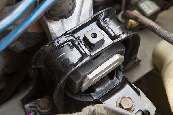 Close-up of a greasy metal engine mount with bolts and blue hoses in a car engine bay | Jeff's Automotive, Inc