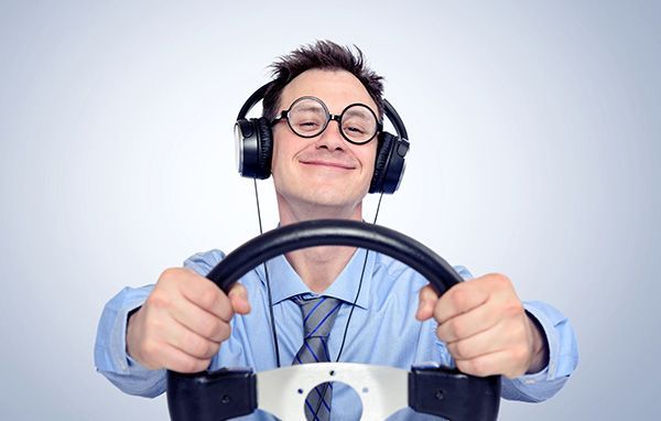 Smiling man wearing headphones, holding a steering wheel controller against a white background | Jeff's Automotive, Inc