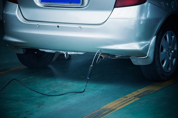 Silver car rear bumper with a dangling cable on a blue garage floor, suggesting a plugged-in electric vehicle | Jeff's Automotive, Inc