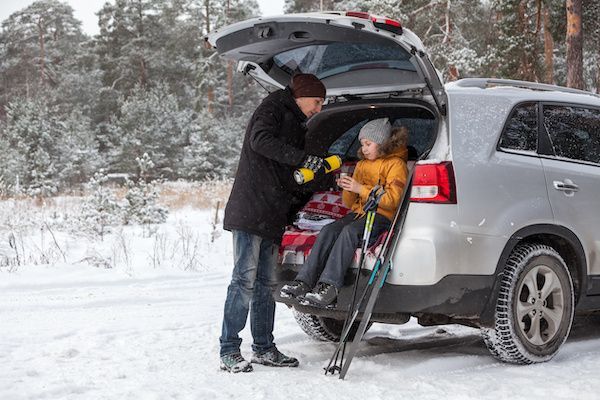 Man loading a bundled dog in a stroller into an SUV on a snowy roadside | Jeff's Automotive, Inc