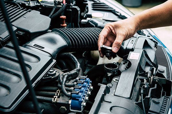 Hand pouring coolant into a car engine reservoir in an open engine bay | Jeff's Automotive, Inc