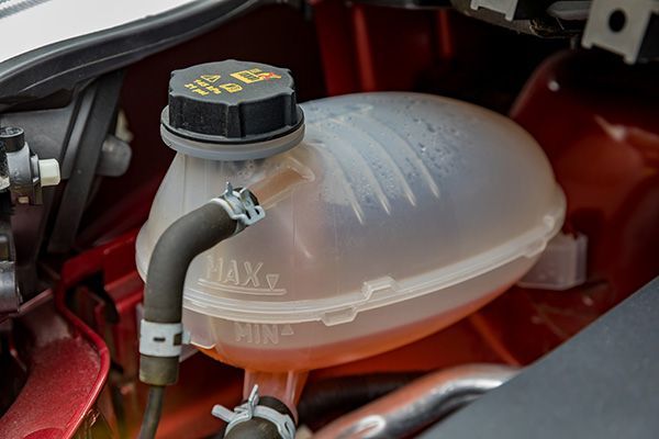 Car engine coolant reservoir with translucent pink fluid and black cap in the engine bay | Jeff's Automotive, Inc