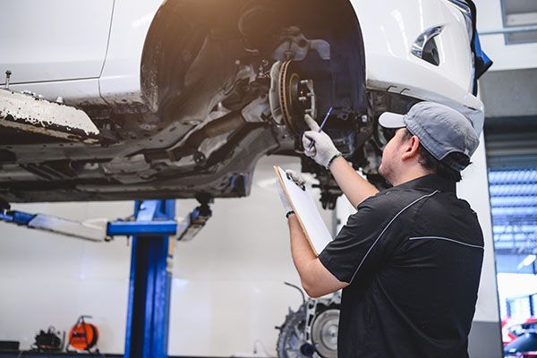 Mechanic inspecting the underside of a white car on a lift in an auto repair shop | Jeff's Automotive, Inc