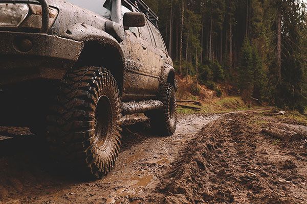 Muddy off-road SUV on a forest trail beside a dirt rut | Jeff's Automotive, Inc