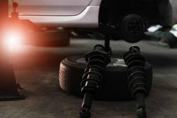 Car wheel, suspension struts, and a bright red light in a dim garage | Jeff's Automotive, Inc