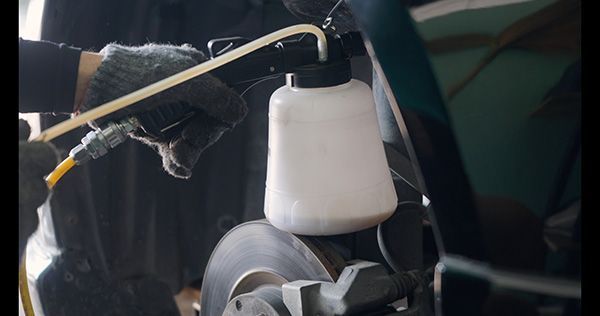 White fluid reservoir and black tubing inside a car engine bay | Jeff's Automotive, Inc