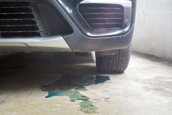 Front of a silver car with green fluid leaking onto a concrete floor. | Jeff's Automotive, Inc
