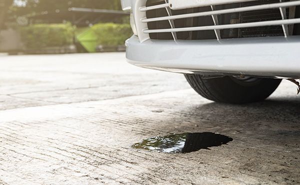 Front bumper of a white car near a pothole on a wet concrete road | Jeff's Automotive, Inc