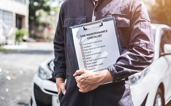 Clipboard checklist held by person beside parked cars outdoors | Jeff's Automotive, Inc