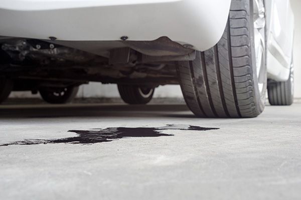 Black fluid leaking under a white car onto a concrete road. | Jeff's Automotive, Inc