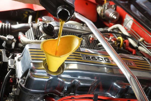 Oil being poured into a car engine through a yellow funnel under the hood. | Jeff's Automotive, Inc