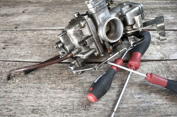 Three carburetors with screwdriver and pliers on a weathered wooden surface | Jeff's Automotive, Inc