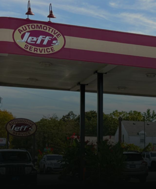 Convenience store gas station with red-and-white canopy and parked cars under a partly cloudy sky