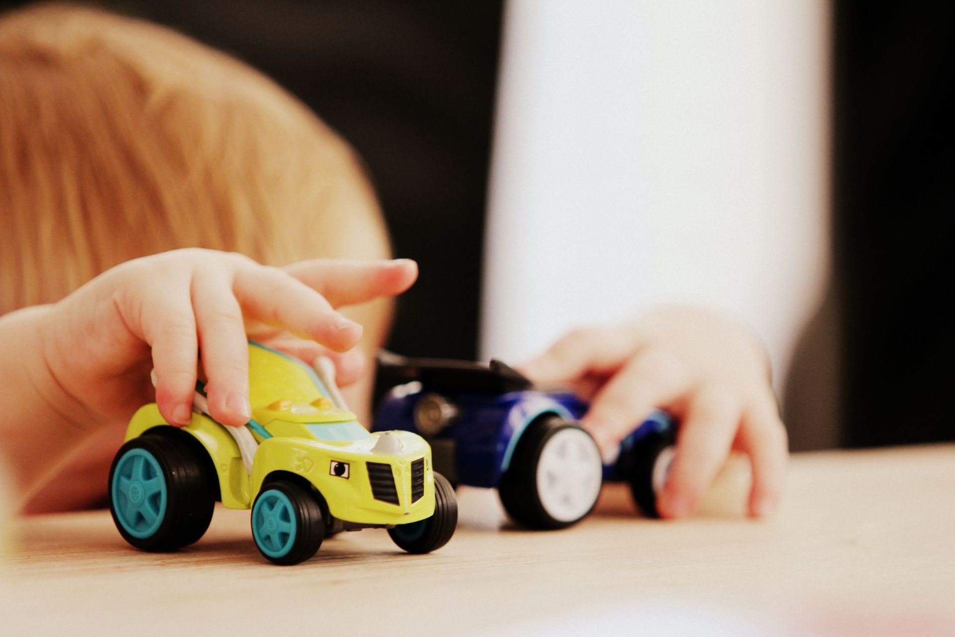 Child’s hands play with yellow and blue toy cars on a table | Jeff's Automotive, Inc
