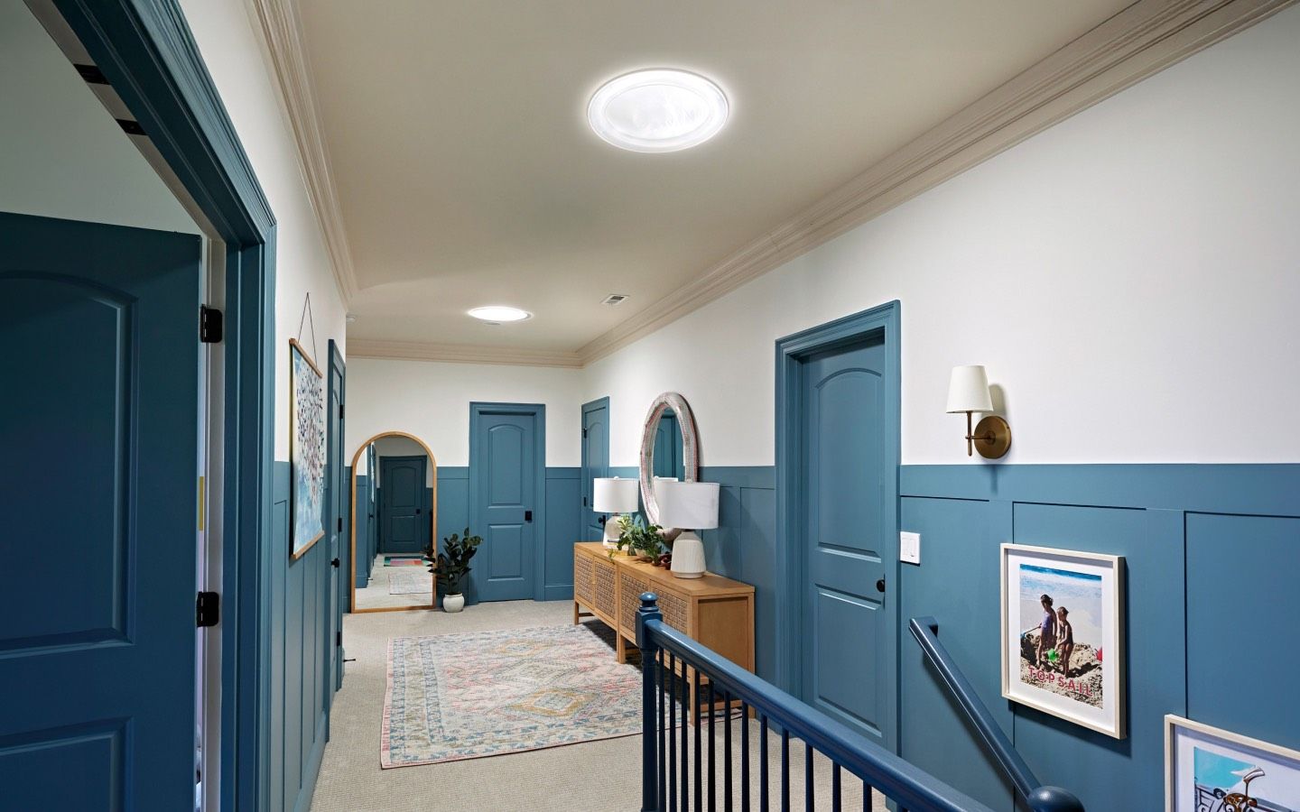 Hallway with blue paneled walls, doors, and skylights in the ceiling.