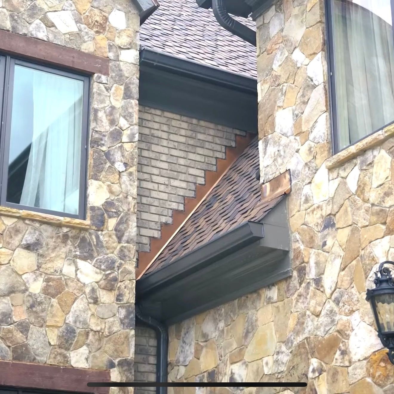 A house exterior featuring a stone-clad wall, a recessed brick section, and a dark-colored roof with metal flashing.